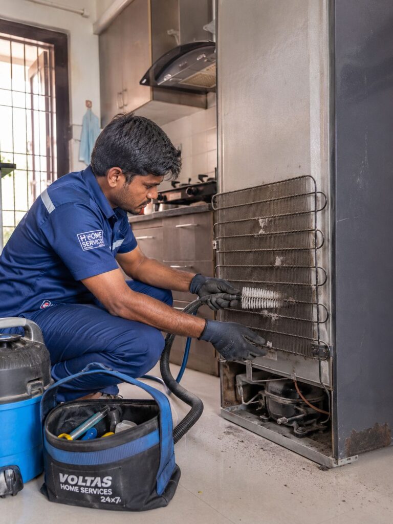 Technician cleaning refrigerator condenser coils in Hyderabad home kitchen